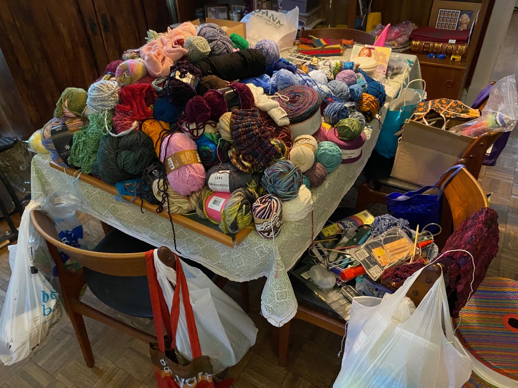 A dining room table is full of yarns, craft supplies, knitting needles and bags of other treasures. You would be right to feel petrified.